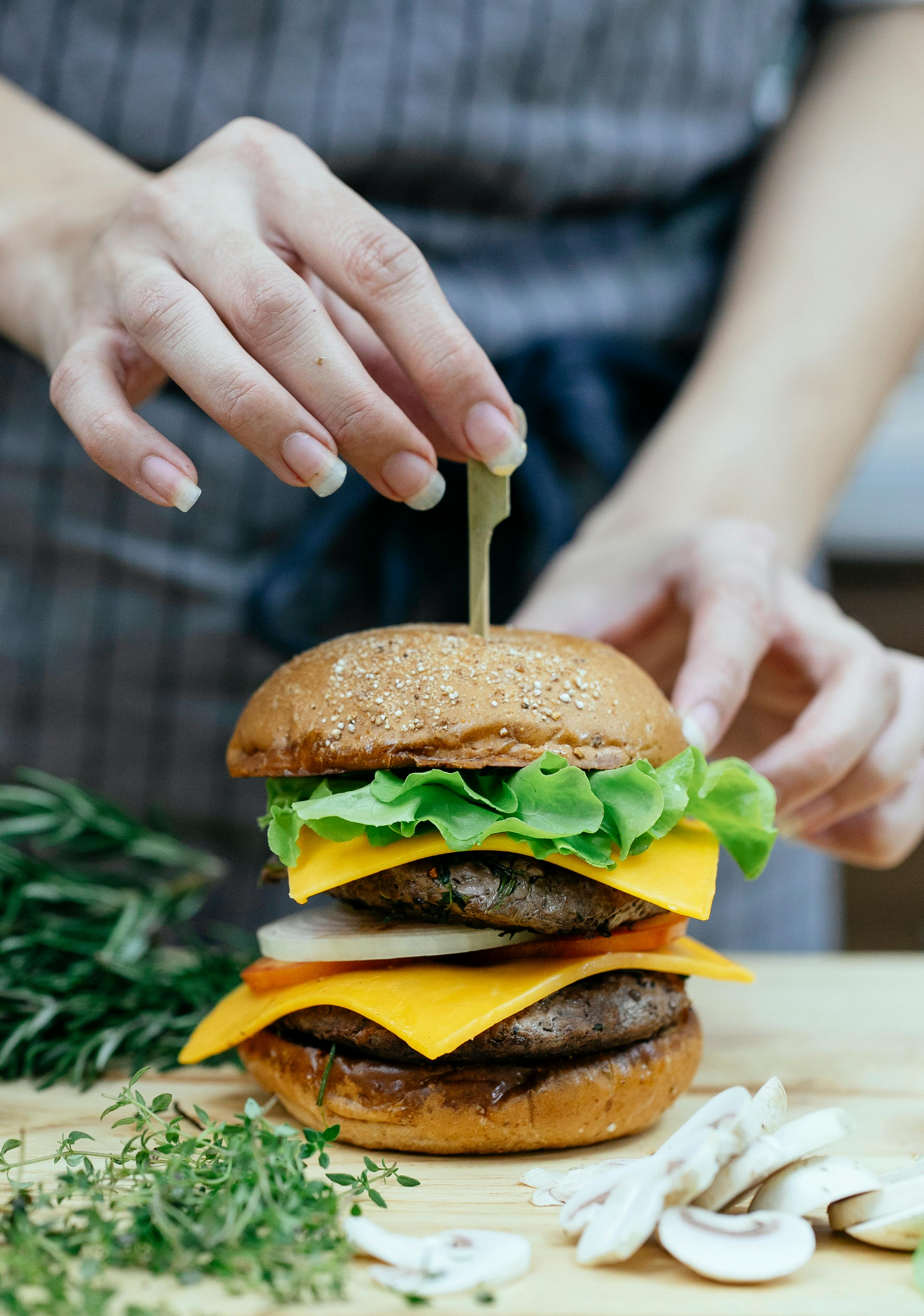 A chef's hands assembling a double cheeseburger topped with fresh lettuce and cheddar cheese.